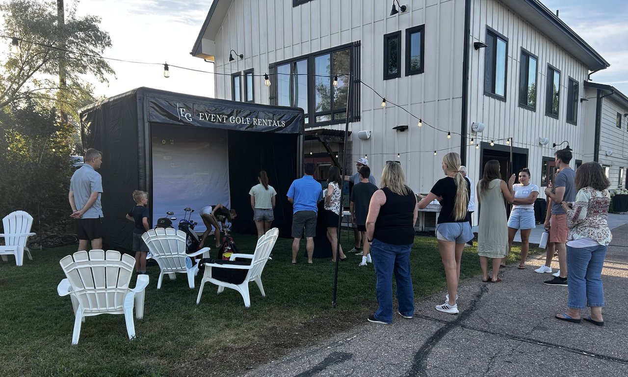 Golf simulator set up in a backyard for an evening party, with guests watching and seating on the lawn