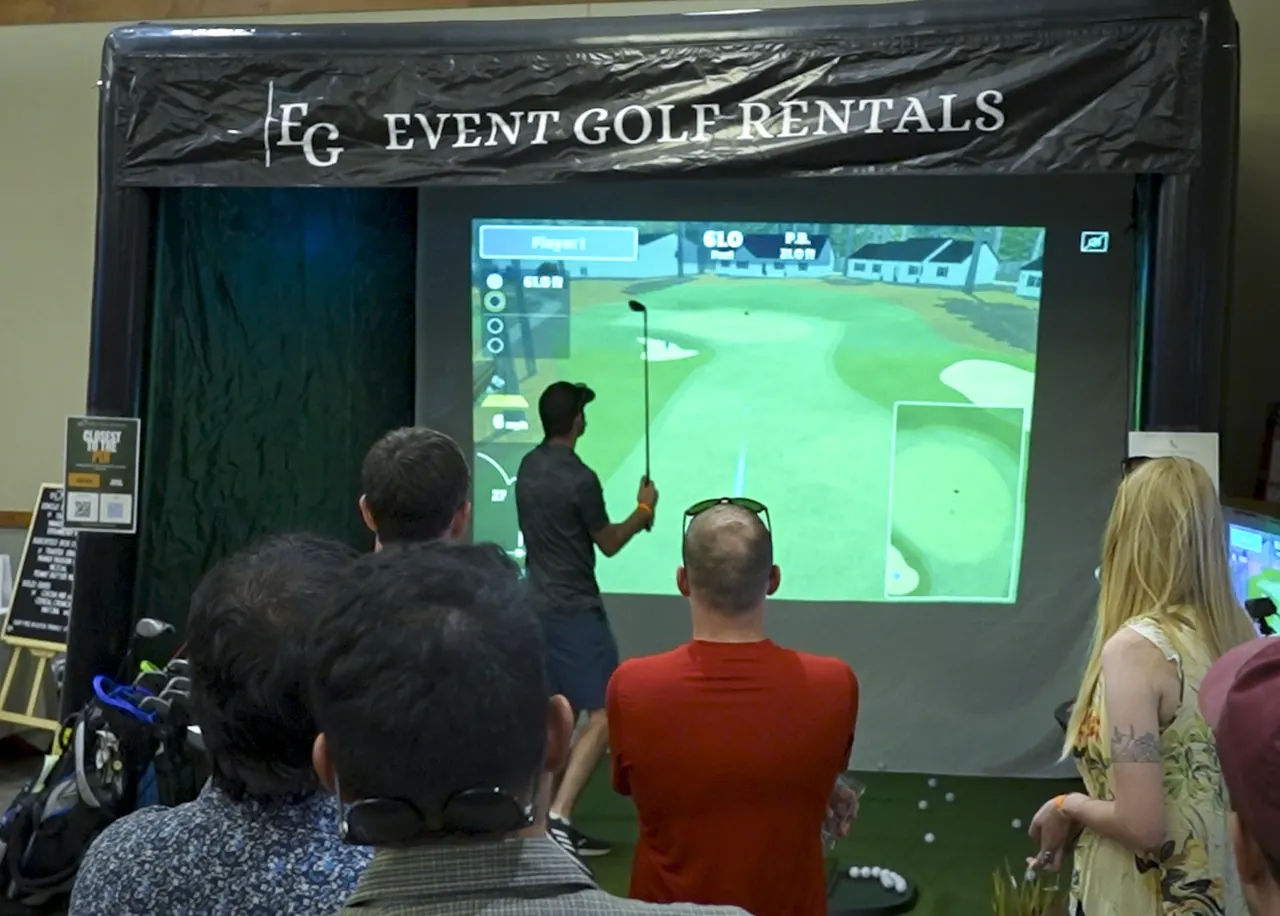 Golf simulator enclosure set up indoors with a crowd of guests watching the screen, showing the full enclosure scale